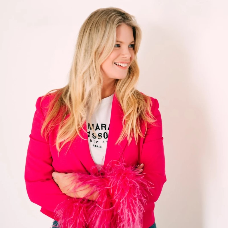 Beth Clay smiling, arms folded, in a bright pink blazer